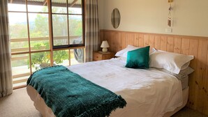 A bedroom with a large bed, a nightstand with a lamp, a window with curtains, and a wall-mounted light fixture. - Mansfield Colonial Cabin with Stunning Views (Mansfield)