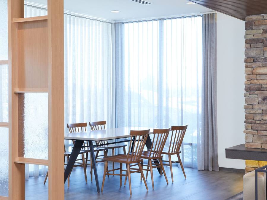 A dining area with a large table and chairs, a stone accent wall, and large windows with curtains.