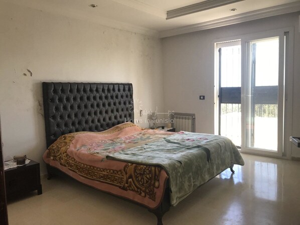 A bedroom with a large bed, a nightstand, and a sliding glass door leading to a balcony.