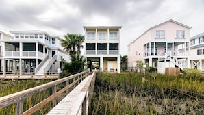 A coastal house with a wooden deck leading to a two-story building with balconies. - Steel Waters – Luxury Deep-Water Retreat with Private Dock & Stunning Marsh Views (Edisto Beach)