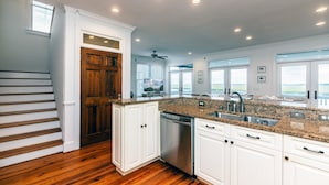 A kitchen with white cabinets, a granite countertop, stainless steel appliances, and a view of the outdoors. - Steel Waters – Luxury Deep-Water Retreat with Private Dock & Stunning Marsh Views (Edisto Beach)