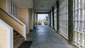 A covered hallway with a staircase on the left, a concrete floor, and large windows on the right. - Steel Waters – Luxury Deep-Water Retreat with Private Dock & Stunning Marsh Views (Edisto Beach)