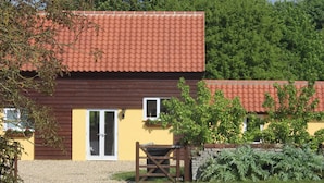 A two-story building with a red-tiled roof, a gravel driveway, and a garden area with plants and a wooden gate.