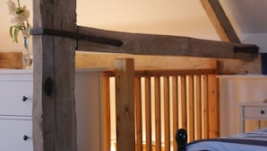 A bedroom with a wooden ceiling, a bed, a dresser, and a window with a view of the outside.