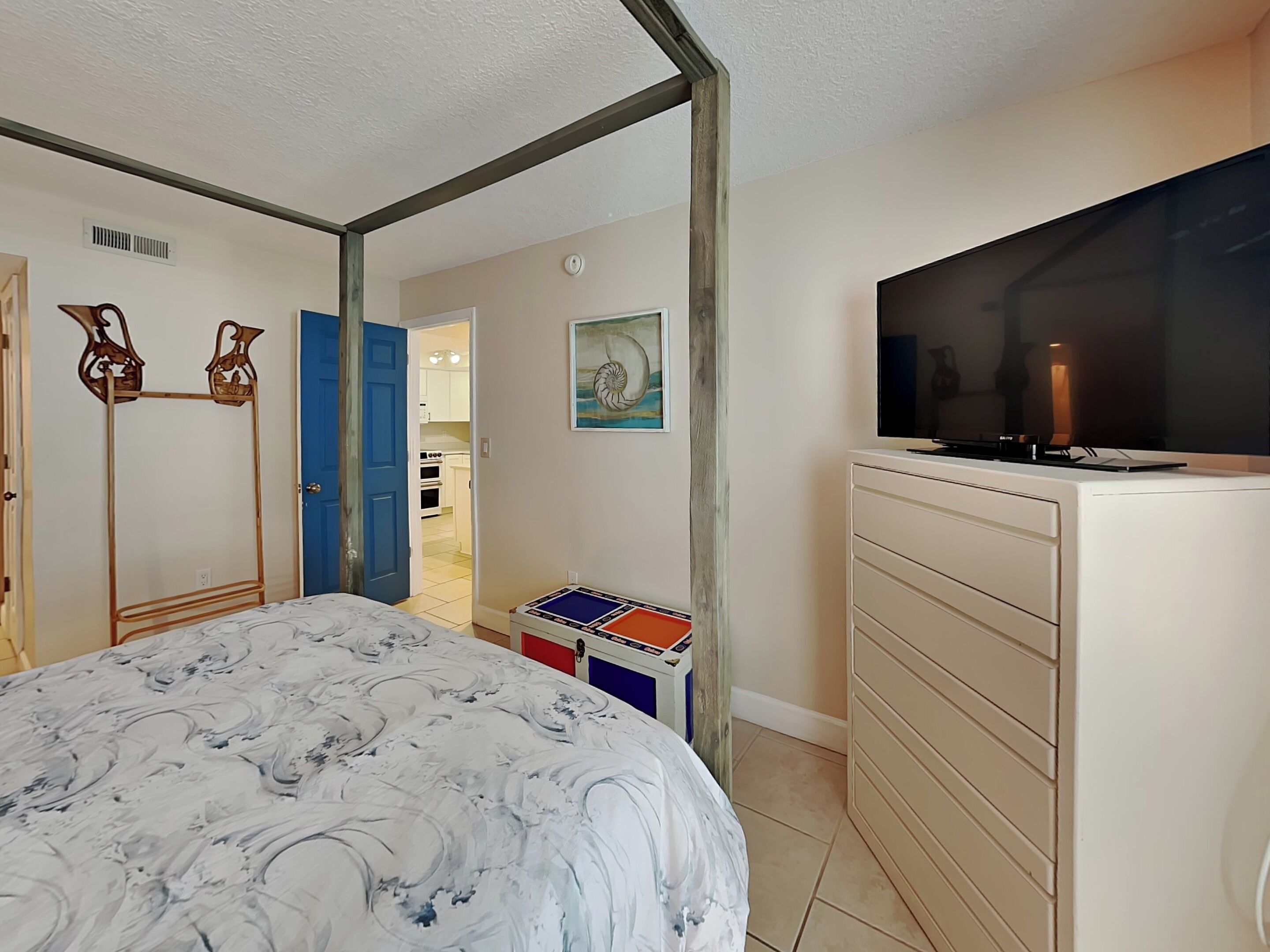 A bedroom with a bed, a TV, a dresser, and a small table with a colorful box.