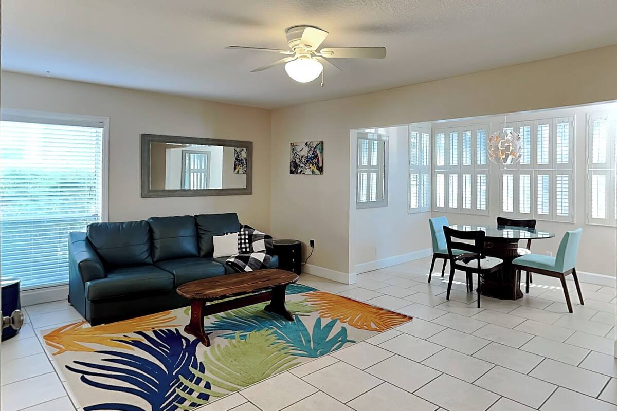 A living room with a dark green sofa, a wooden coffee table, and a dining area with a glass table and chairs.
