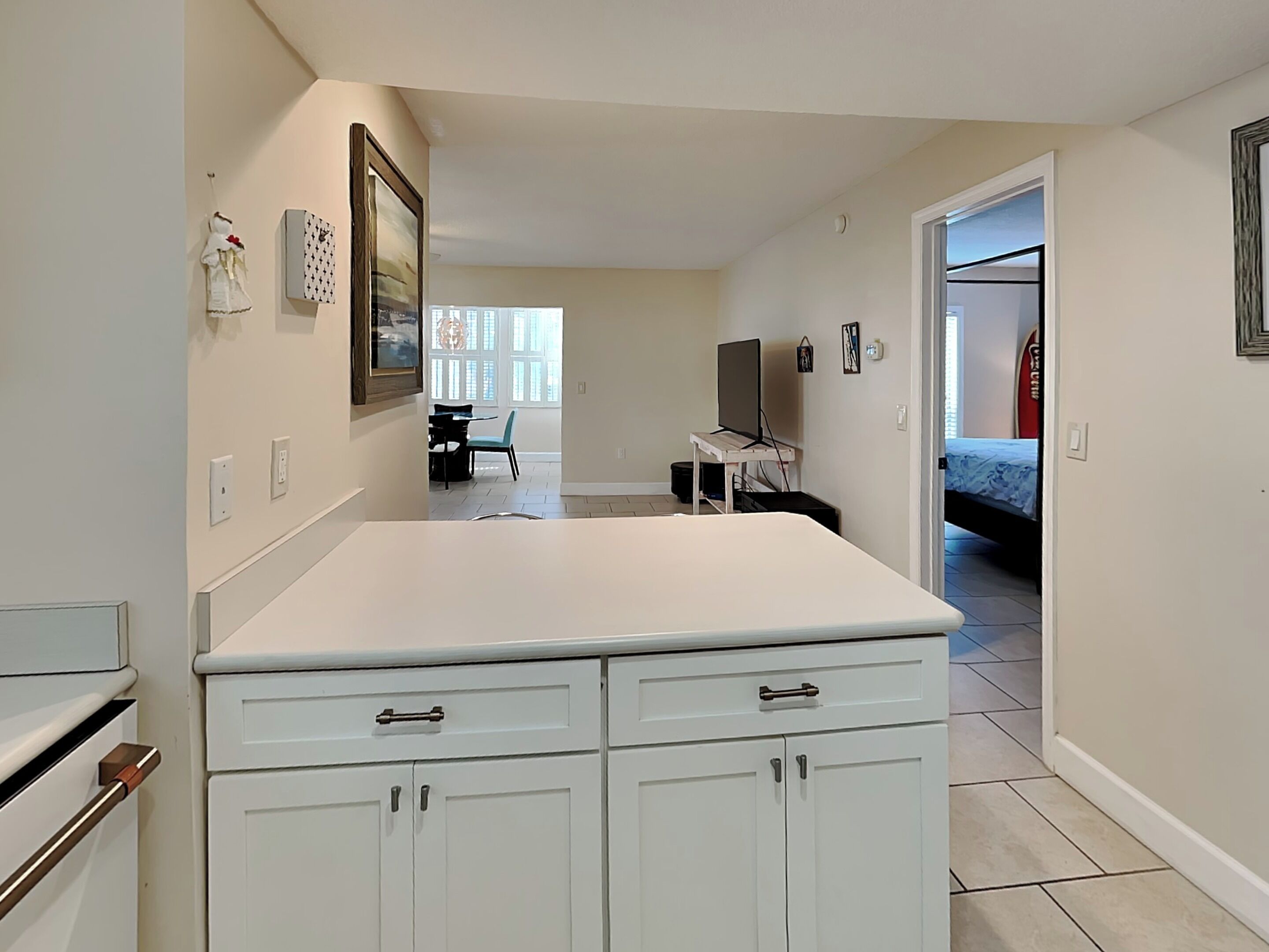 A modern kitchen with white cabinetry, a dining area with a table and chairs, a TV, and a bed in the adjacent room.