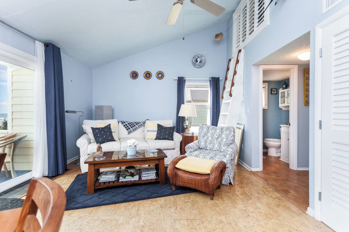 A living room with a white sofa, a patterned armchair, a coffee table with magazines, and a blue wall with decorative plates.