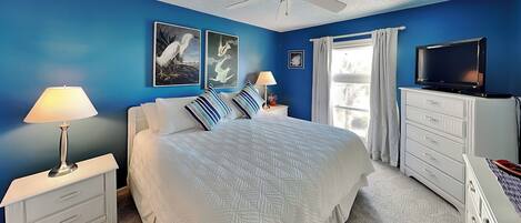 A bedroom with a bed, nightstands, a TV, and artwork on the walls.