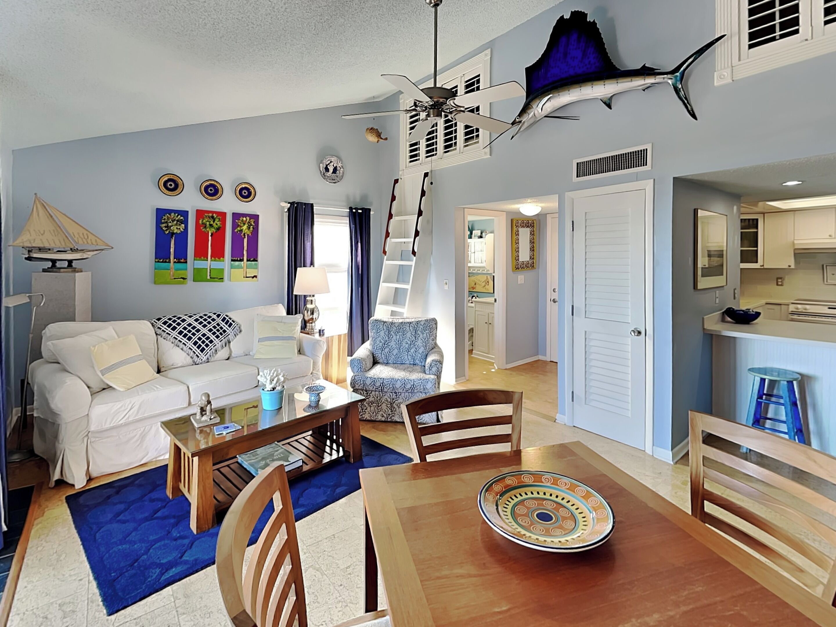 A living room with a dining table, chairs, a sofa, a lamp, and a ceiling fan.
