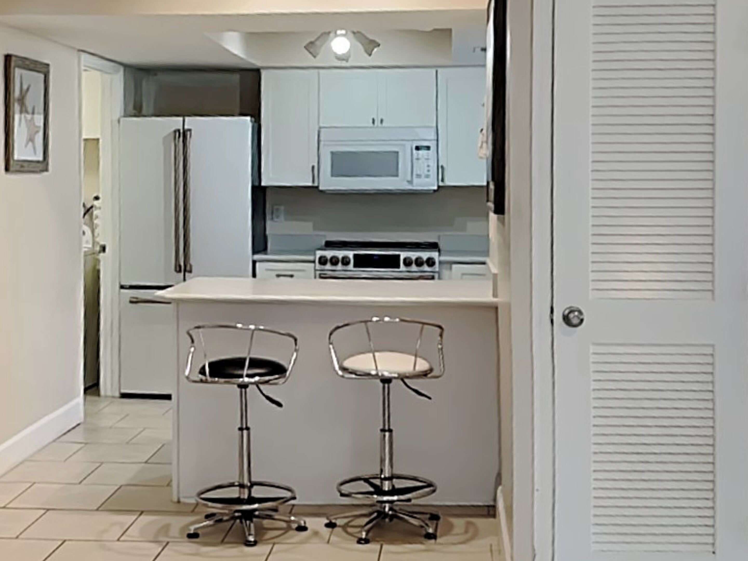 A compact kitchen with a microwave, stove, and two bar stools.
