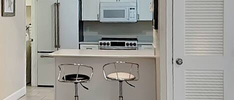 A compact kitchen with a microwave, stove, and two bar stools.