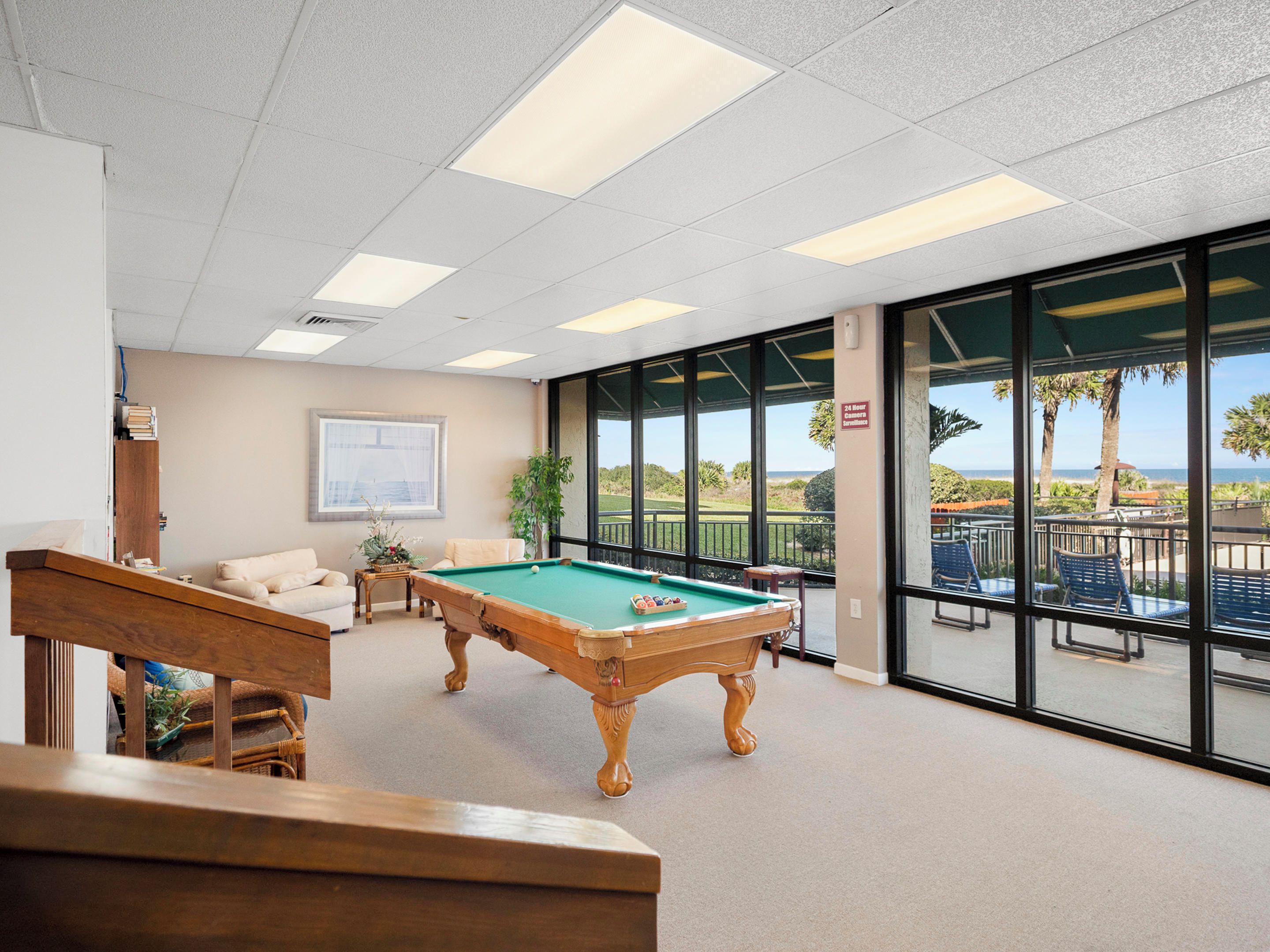 A pool table in a room with large windows, a staircase, and a view of the ocean.