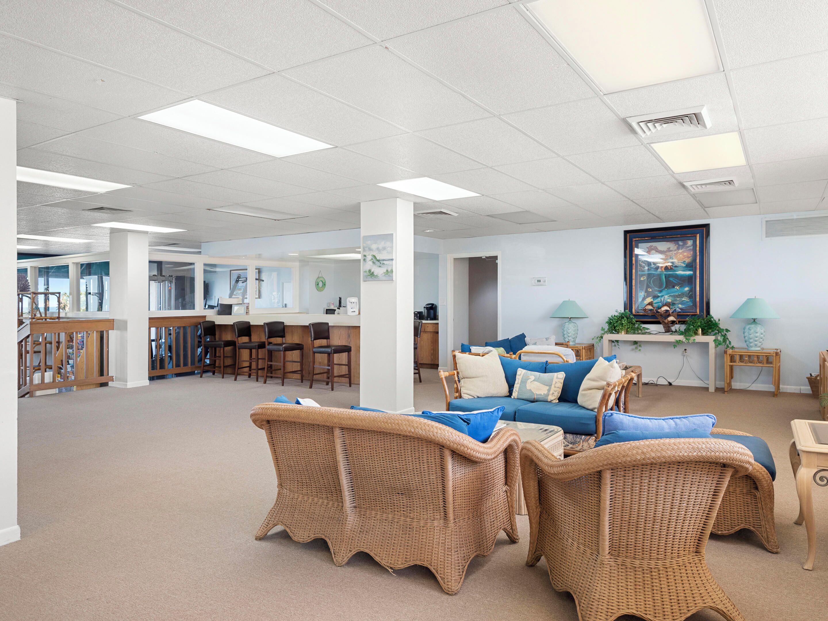 A spacious room with a large sofa, wicker chairs, a bar area, and a painting on the wall.
