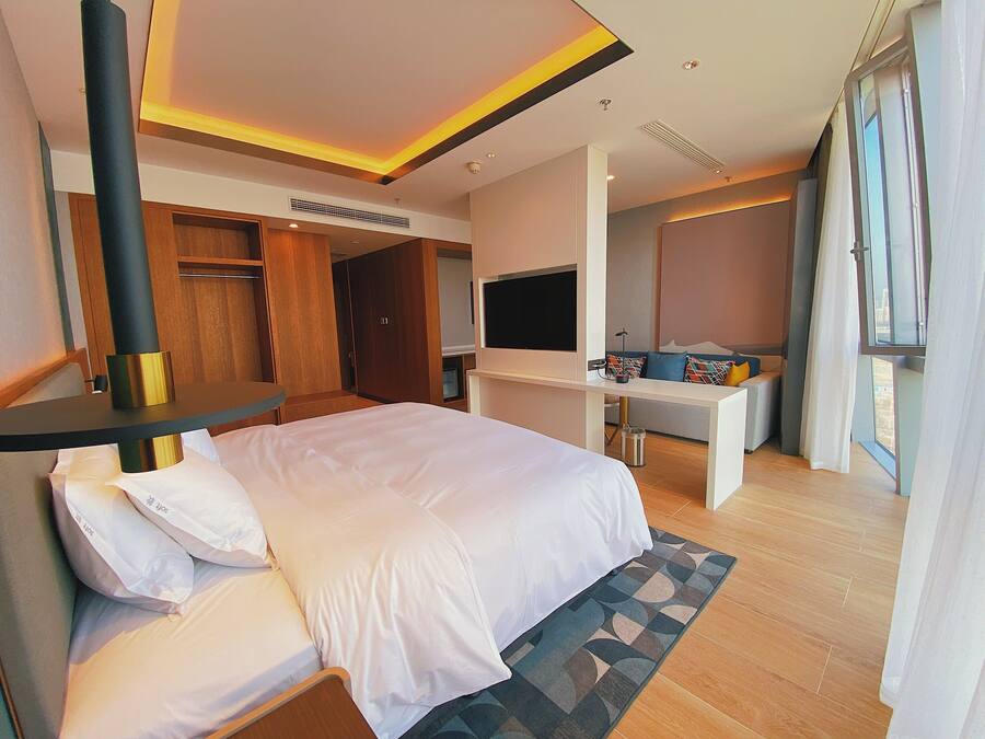 A modern hotel room with a large bed, a desk, a TV, and a wardrobe.