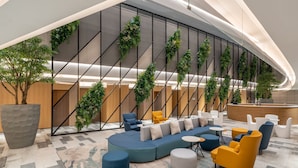 Un vestíbulo moderno con techo curvo, una recepción, un área de estar con sofás y sillones, y jardines verticales.