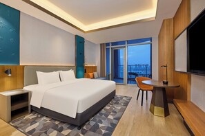 Moderni hotellihuone, jossa on suuri sänky, työpöytä, tuoli ja parveke, jolta on näkymä.