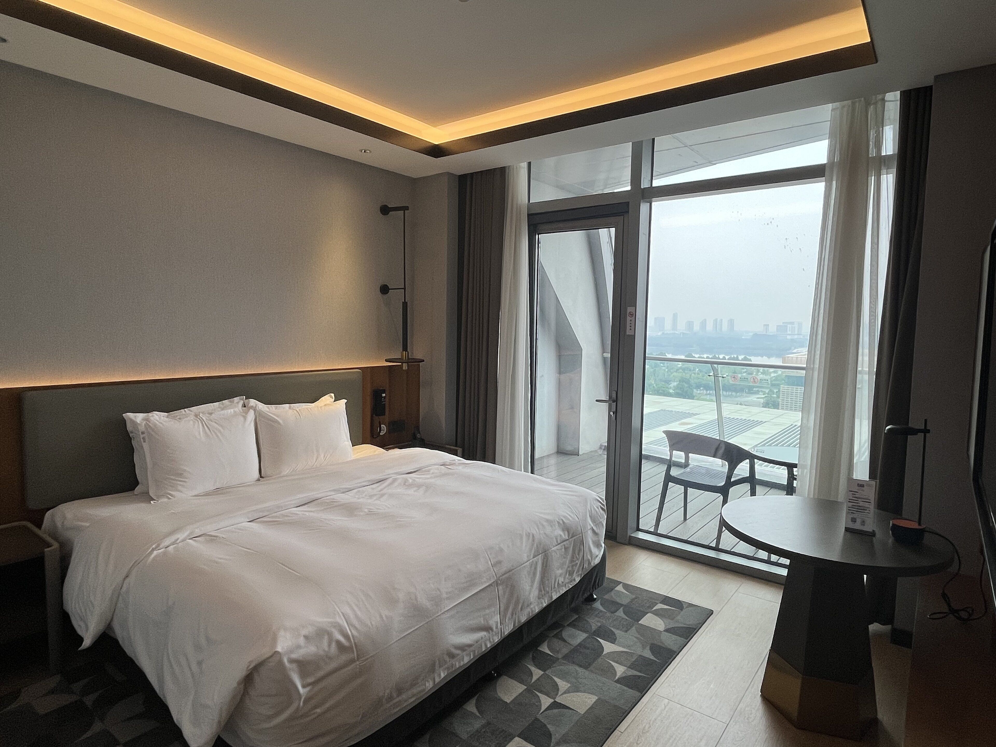 Una habitación de hotel moderna con una cama grande, un escritorio y un balcón con vistas a la ciudad.
