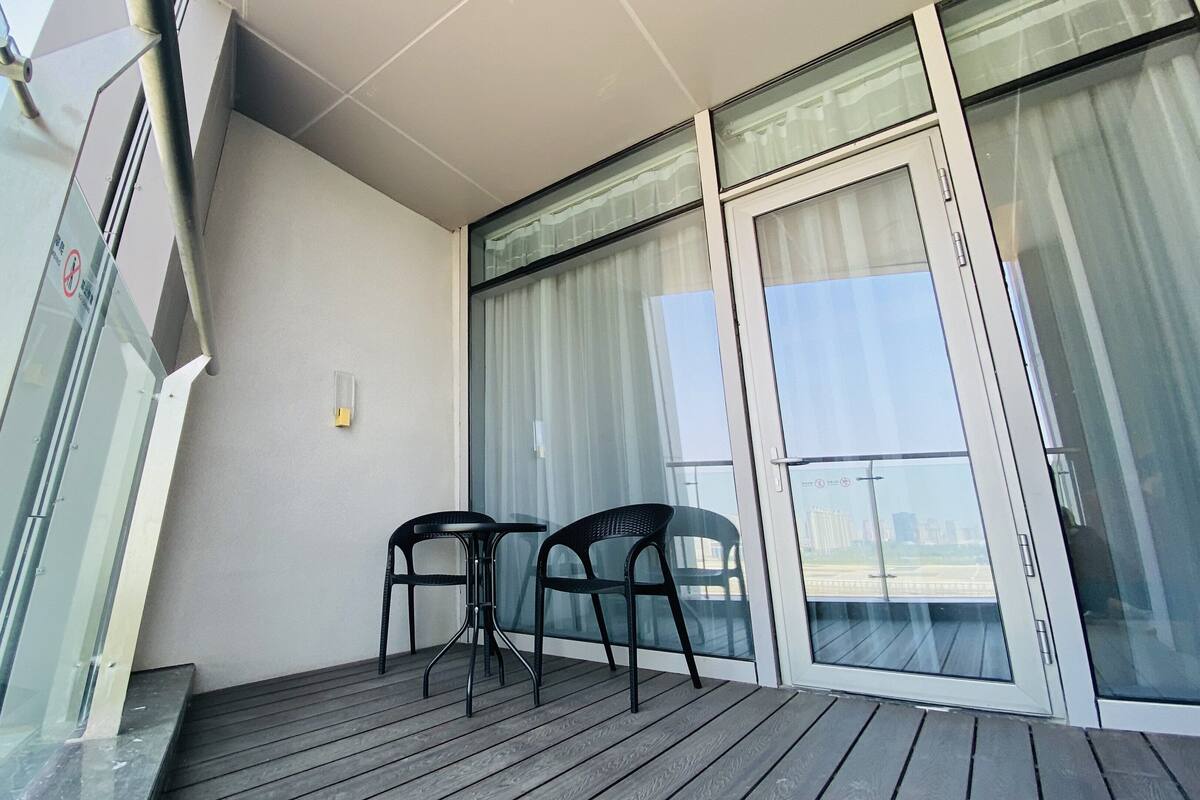 A balcony with two chairs, a glass door, and a view of buildings.