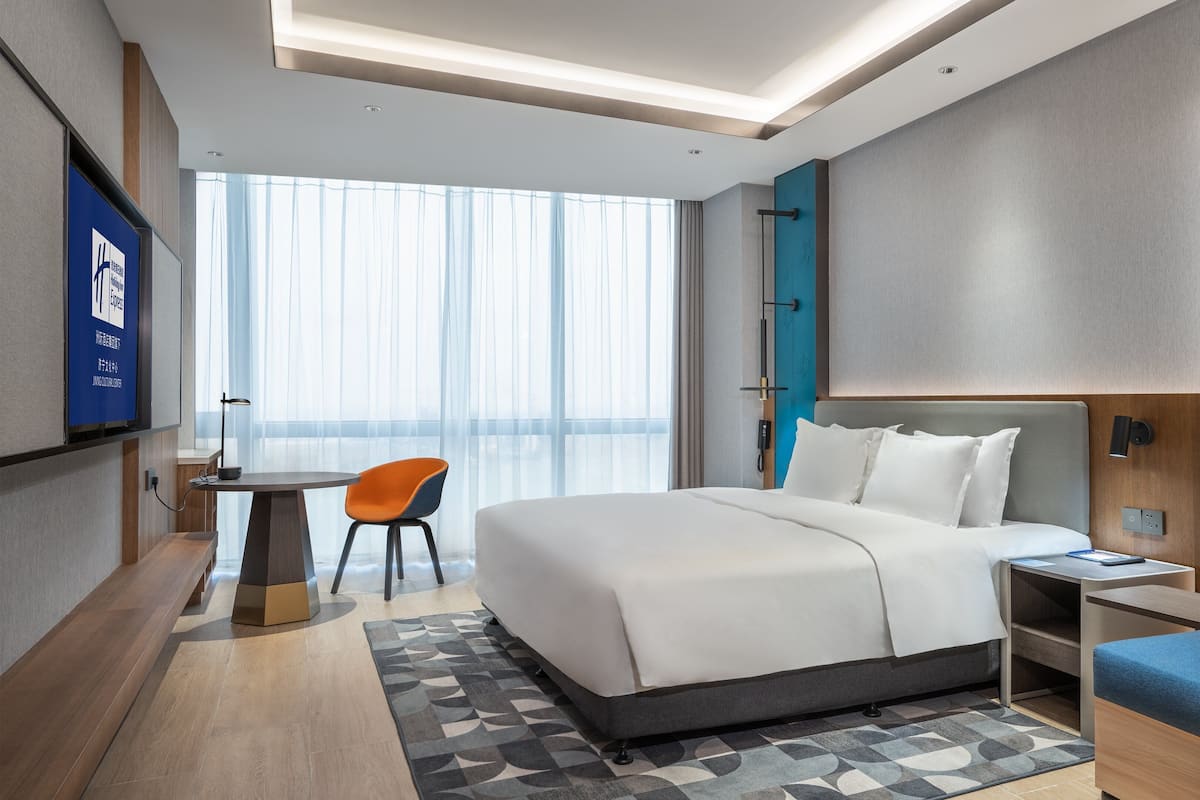 A modern hotel room with a large bed, a desk with a chair, a TV, and a sofa.