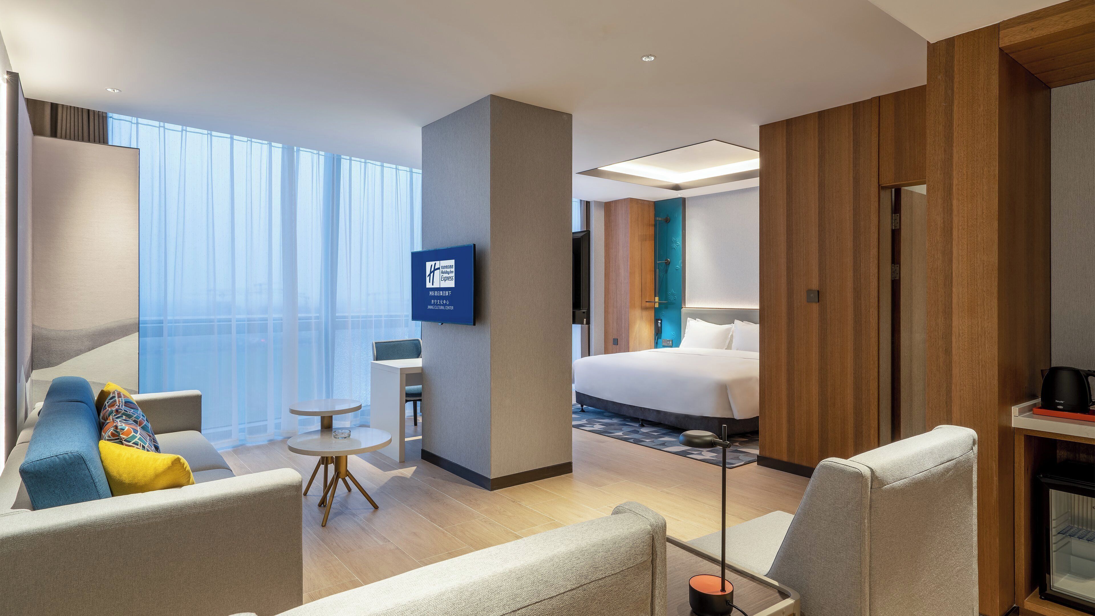 A hotel room with a bed, a desk, a chair, a small table, and a television.