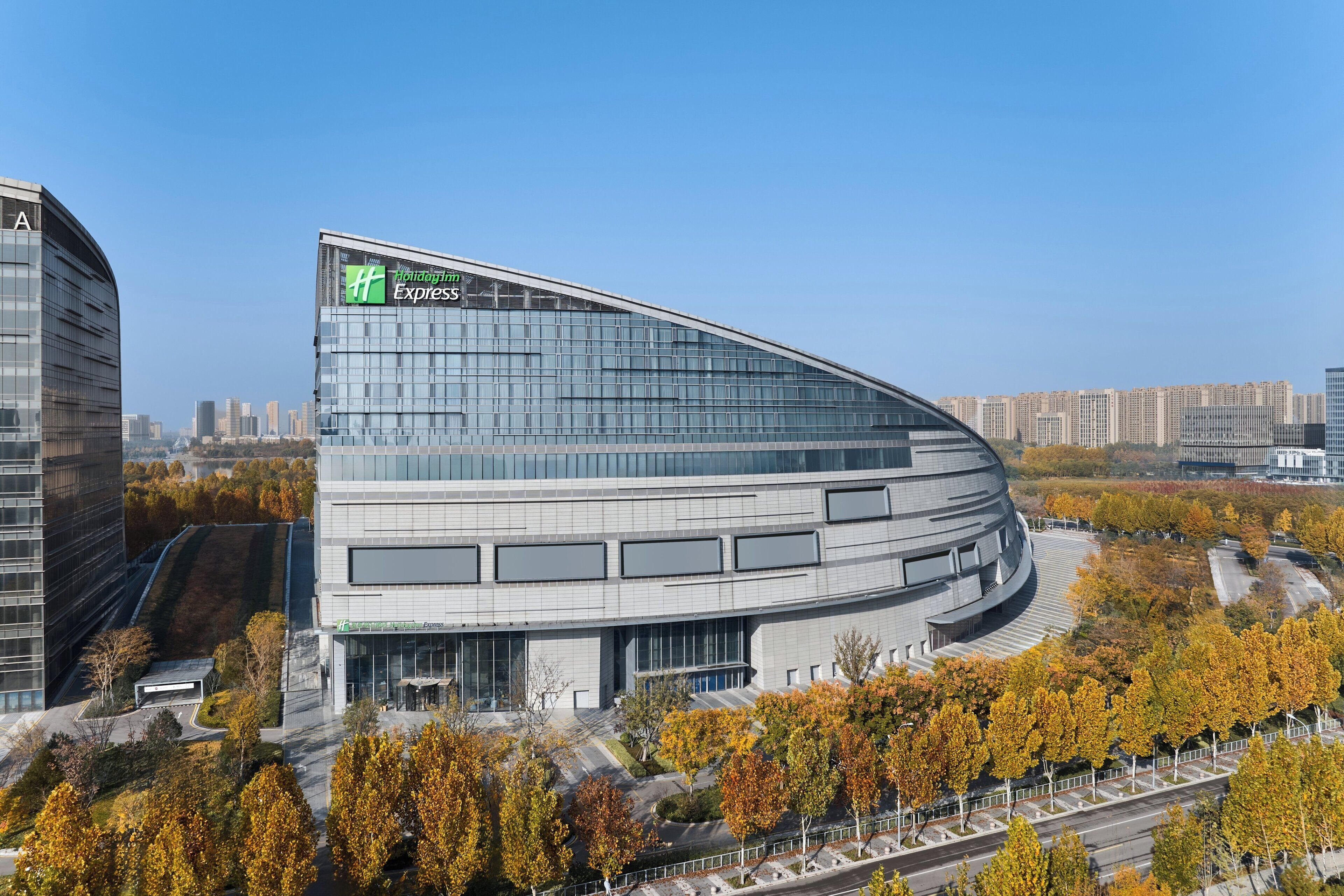 Een modern gebouw met een gebogen gevel, grote ramen en een groen logo bovenaan.