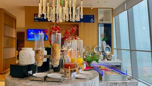 Un bufé de desayuno con diversas opciones de comida, una máquina de café y un televisor al fondo.
