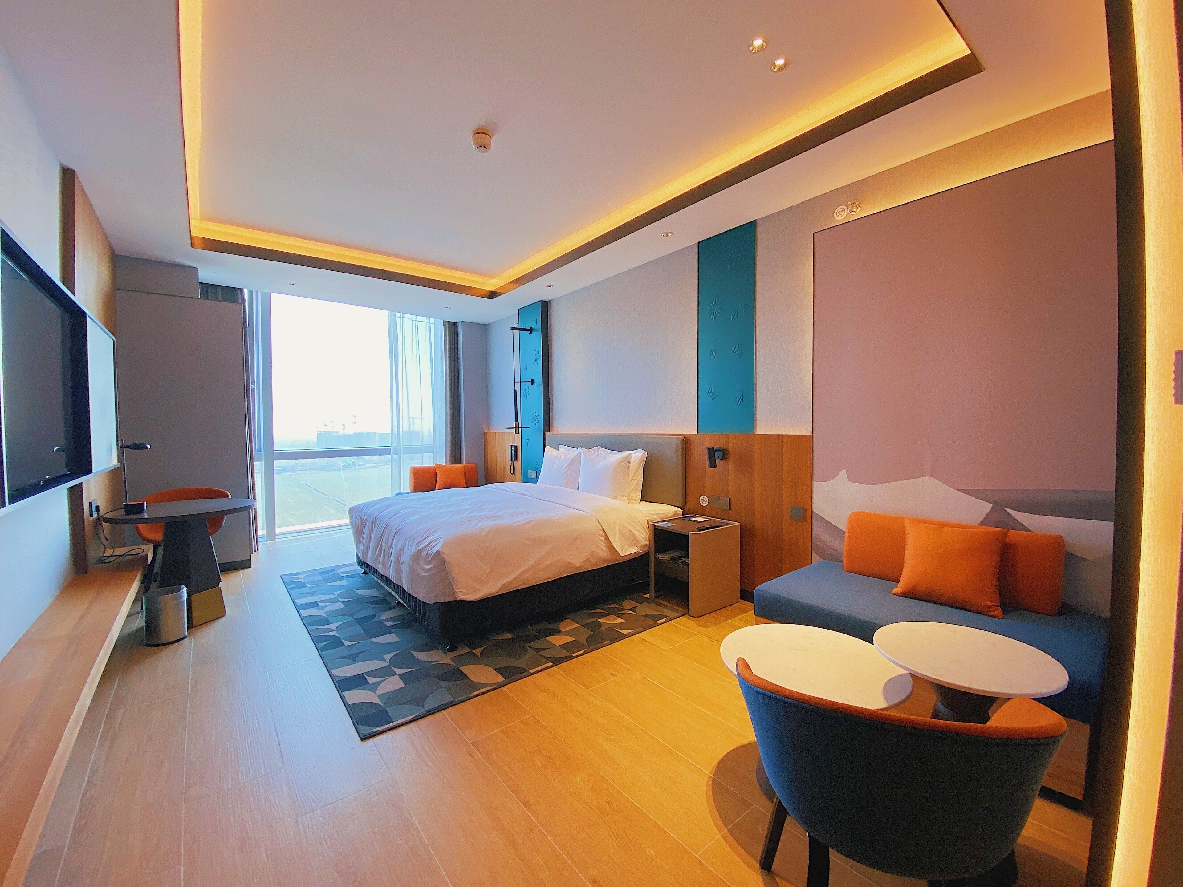 A modern hotel room with a large bed, a desk, a chair, and a sofa.