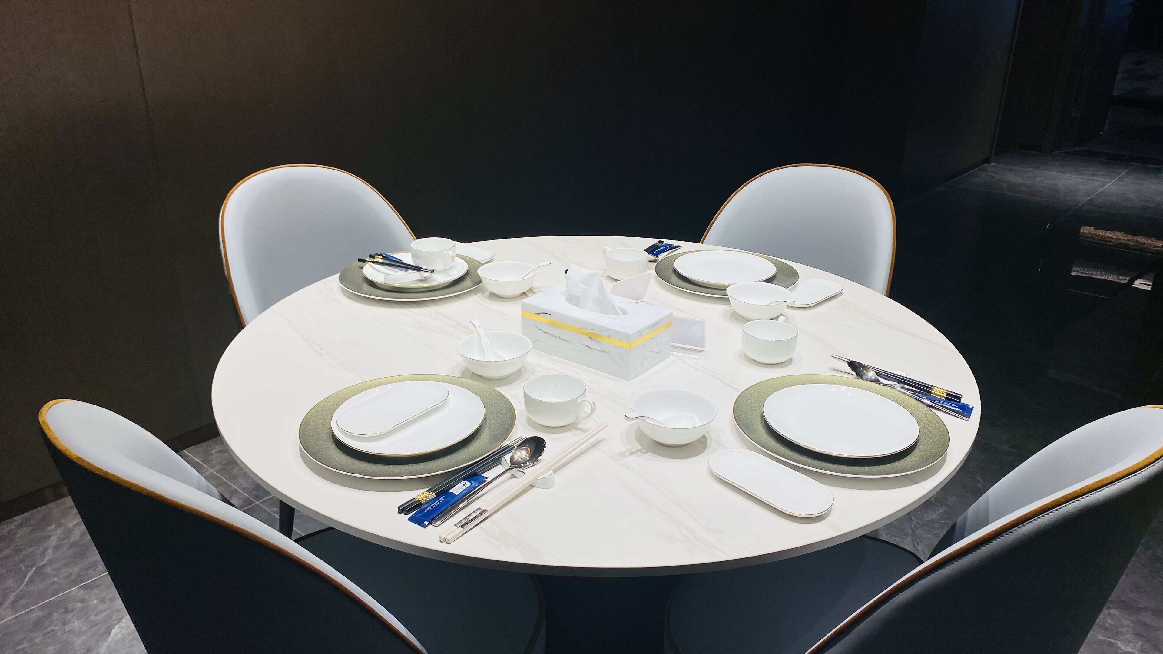 Una mesa redonda de comedor con platos, cuencos y cubiertos blancos, rodeada por cuatro sillas.