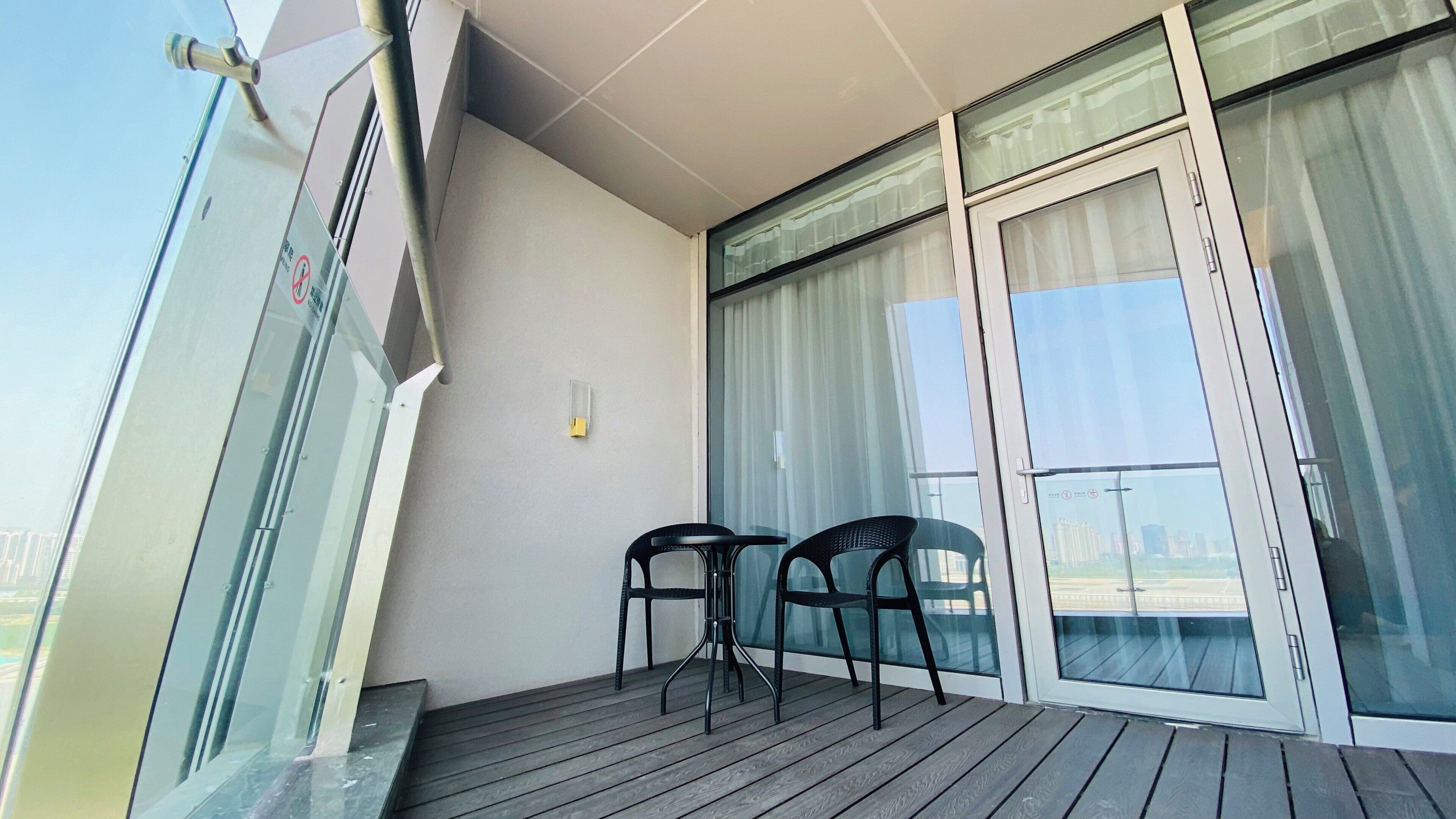 A balcony with a wooden floor, two chairs, and a glass door with curtains.