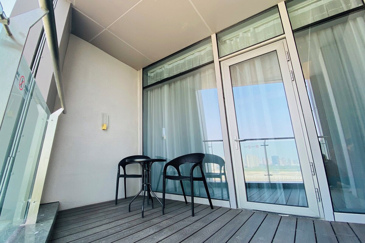 A balcony with a wooden floor, two chairs, and a glass door with curtains.