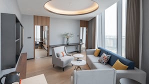 Habitación de hotel moderna con sofá, sillón, mesa de comedor y un ventanal con vista a la ciudad.