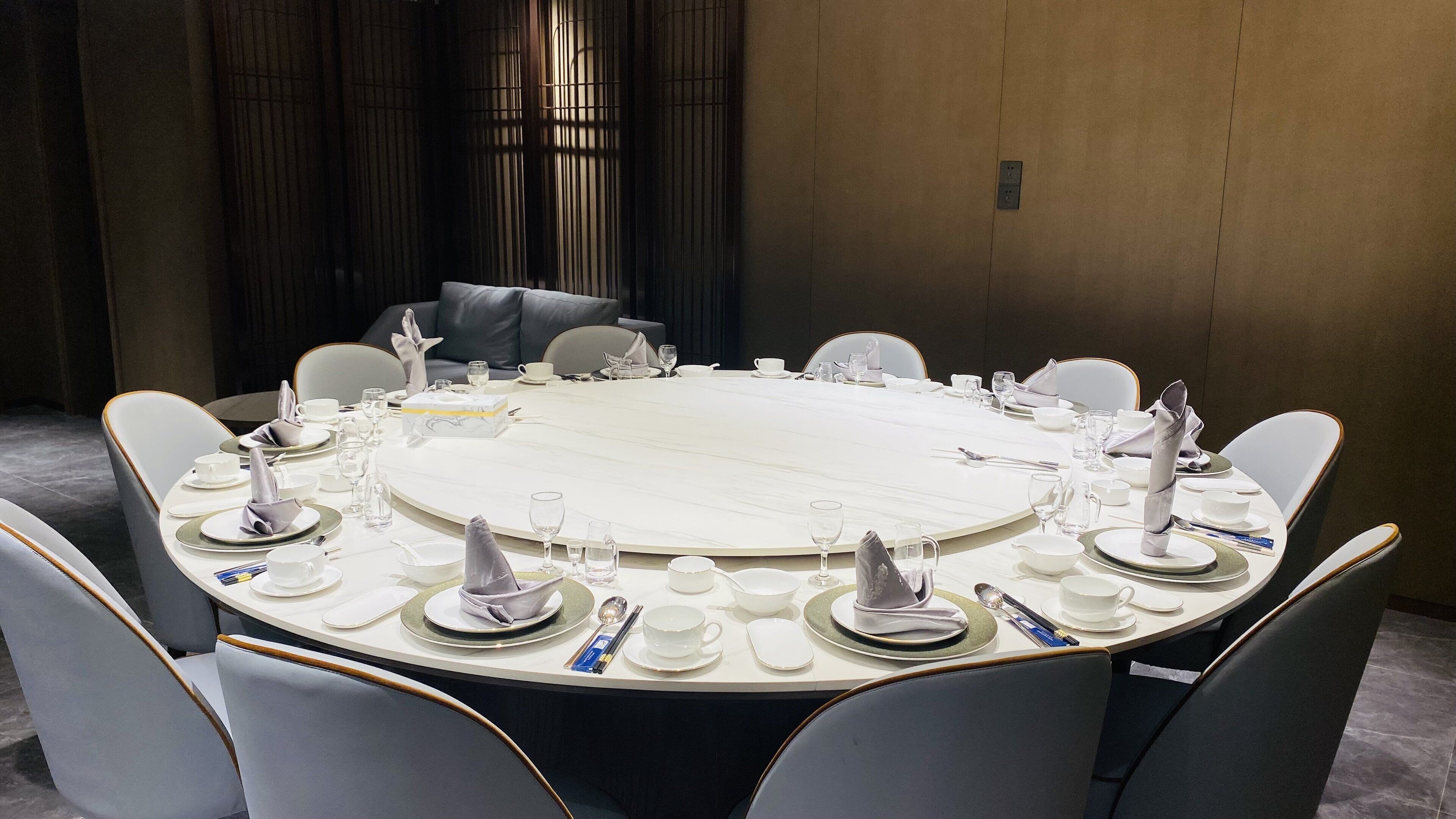 Une table de conférence ronde, recouverte de nappes blanches, entourée de chaises grises à revêtement en tissu.