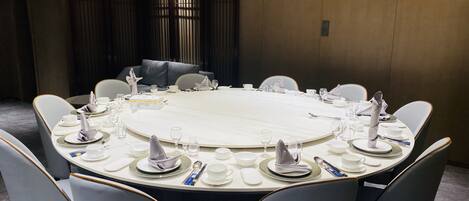 Une table de conférence ronde, recouverte de nappes blanches, entourée de chaises grises à revêtement en tissu.