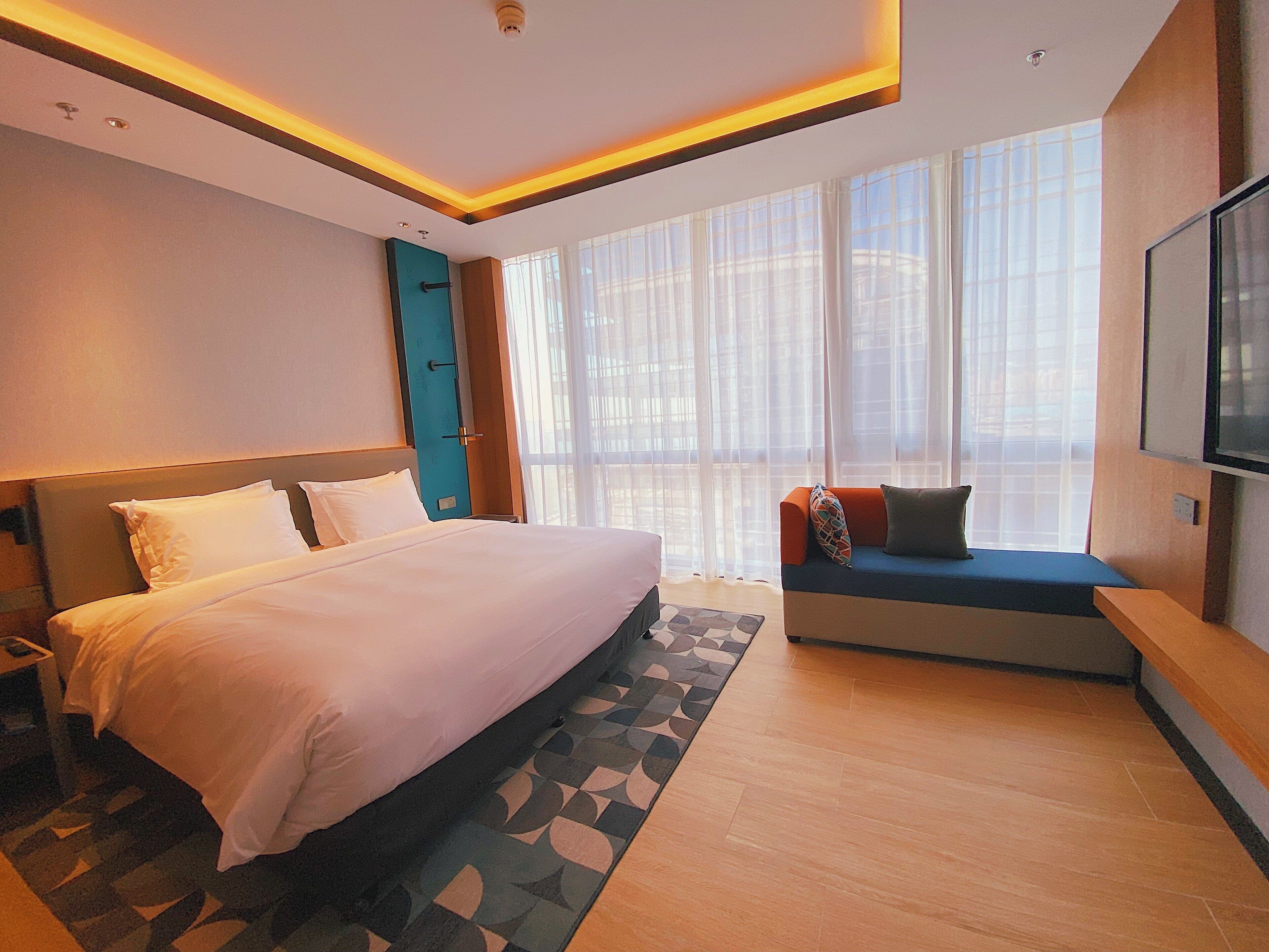 A modern hotel room with a large bed, a sofa, and a TV.