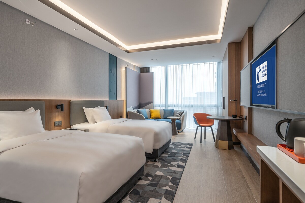 A hotel room with two beds, a desk, a chair, and a television.