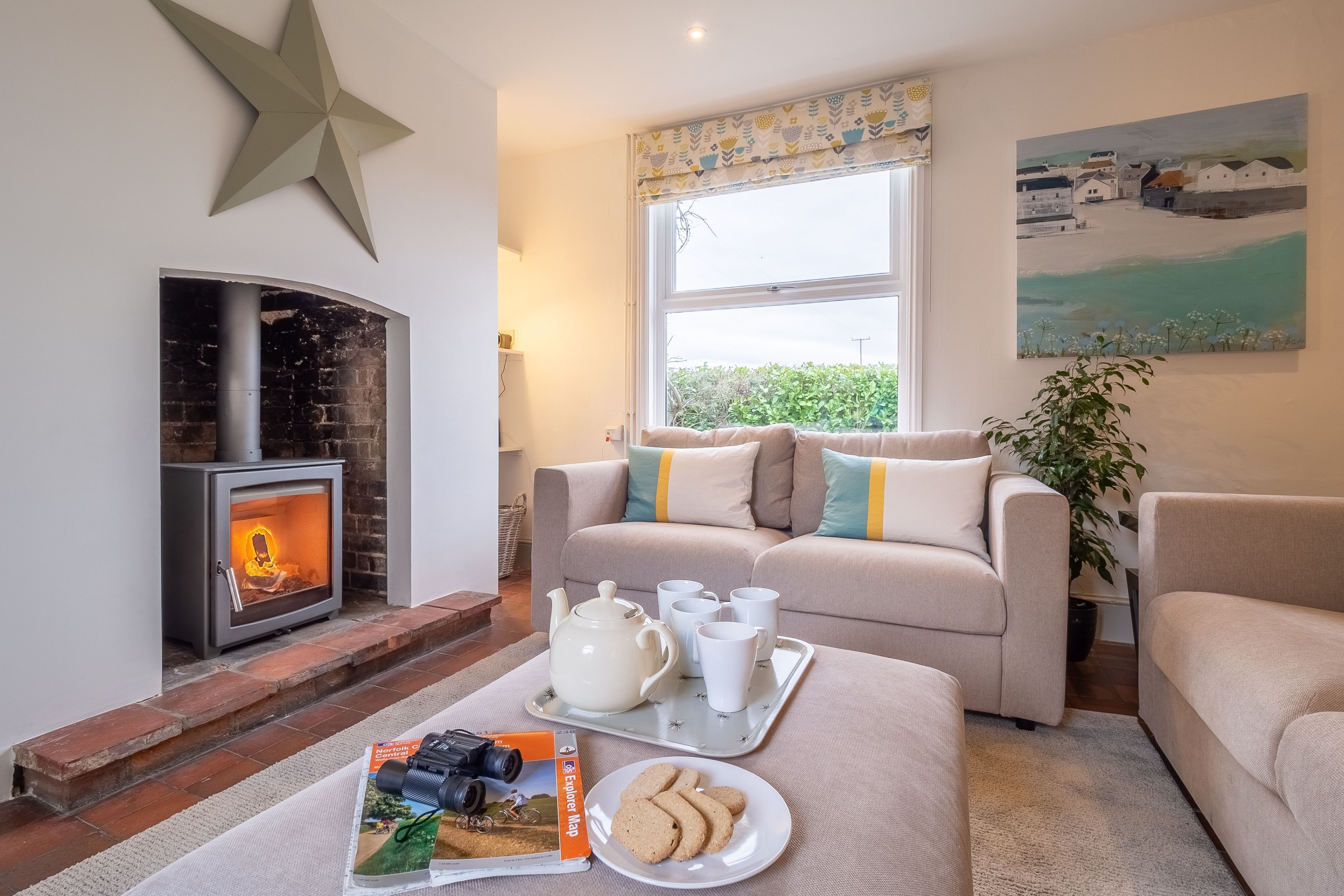 A cozy living room with a fireplace, a sofa set, a tray with teapot and cups, and a magazine.