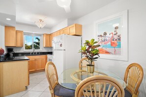 A modern kitchen with wooden cabinets, a white refrigerator, a glass dining table with chairs, and a potted plant. - Waves by Distinctive Beach Rentals (St. Pete Beach)