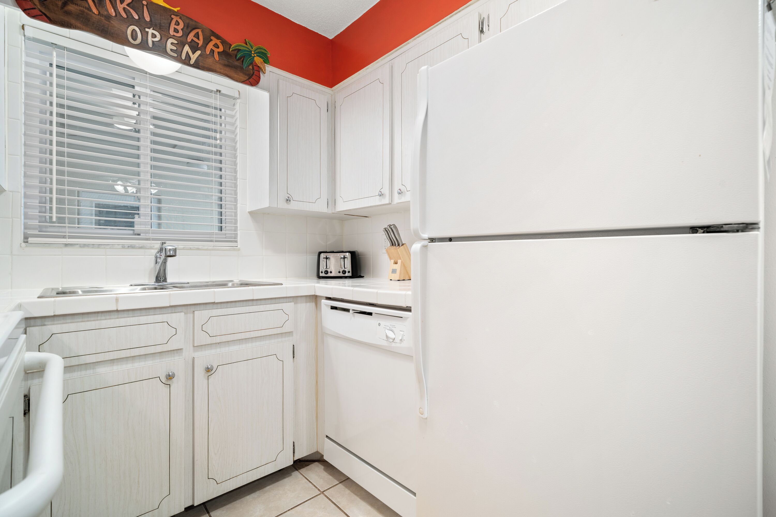 A kitchen with white cabinets, a refrigerator, a sink, and a window with blinds.