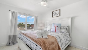 A bedroom with a bed, a window with curtains, a ceiling fan, and a framed quote on the wall. - Waves by Distinctive Beach Rentals (St. Pete Beach)