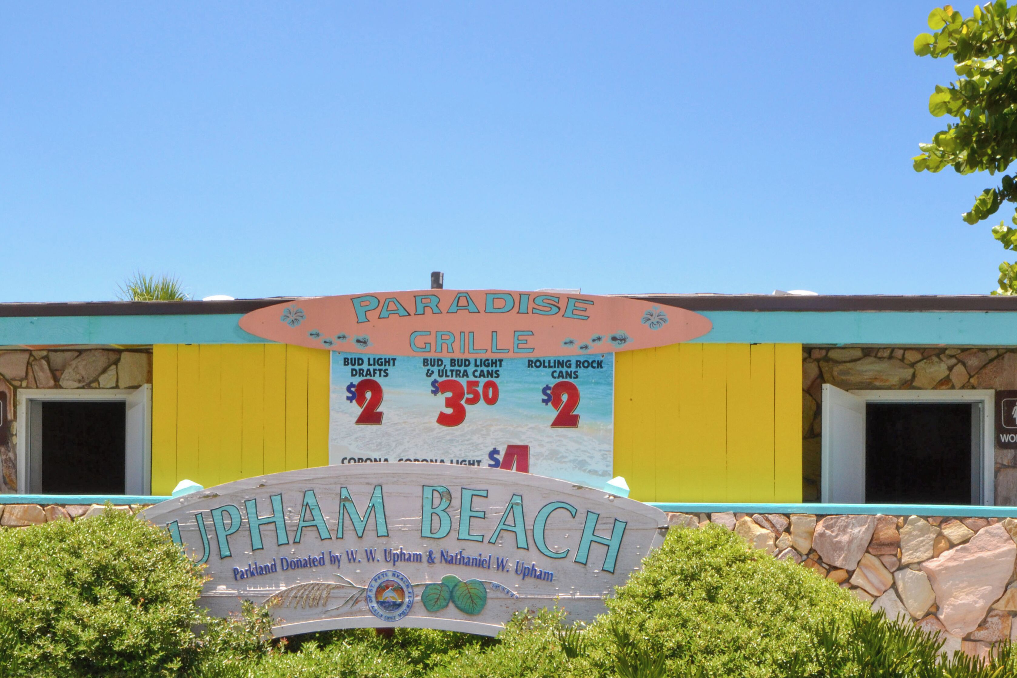 Schild für Paradise Grill am Upham Beach, zeigt eine Steinmauer und einen strahlend blauen Himmel.