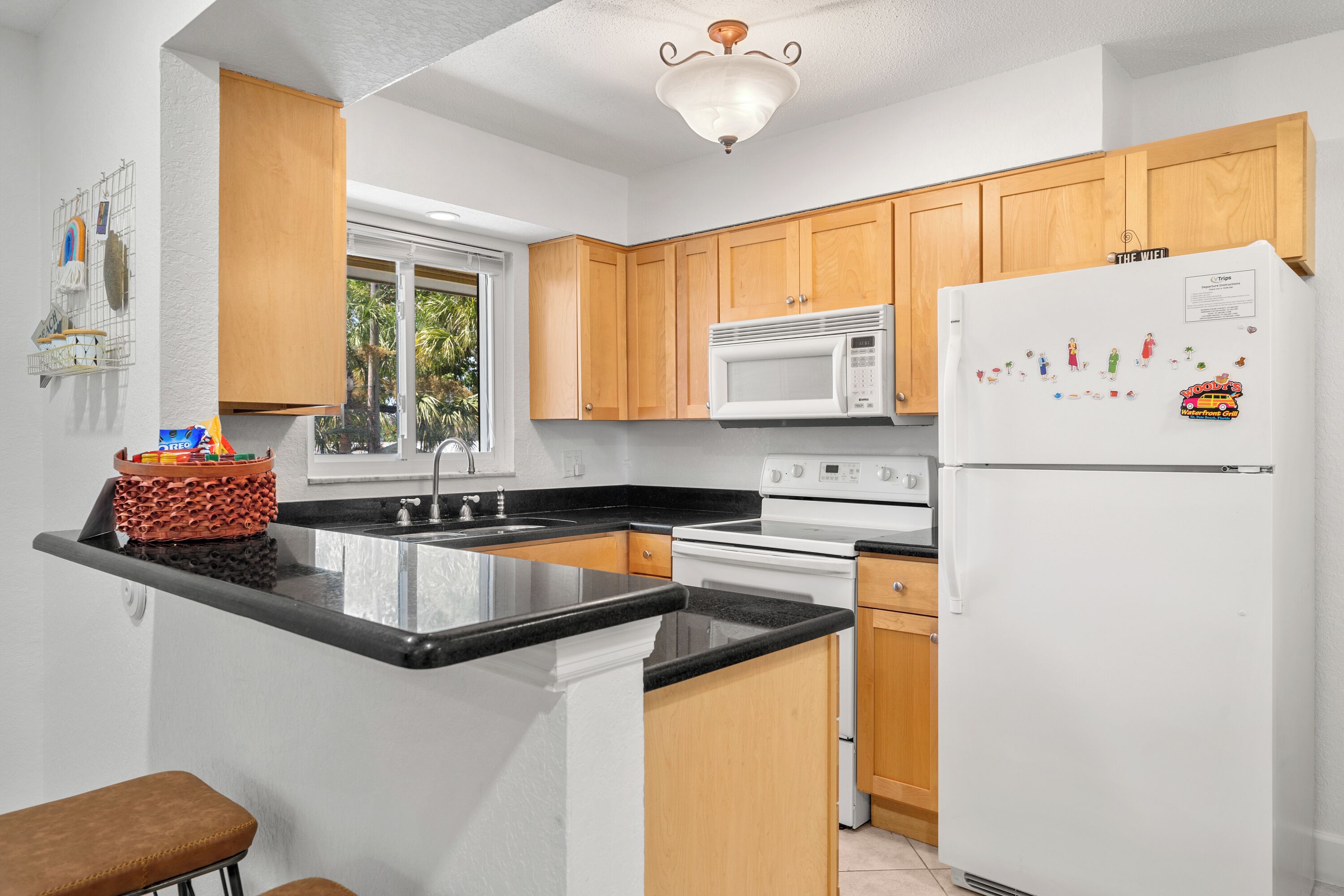 A modern kitchen with wooden cabinets, a white refrigerator, a microwave, and a large window.