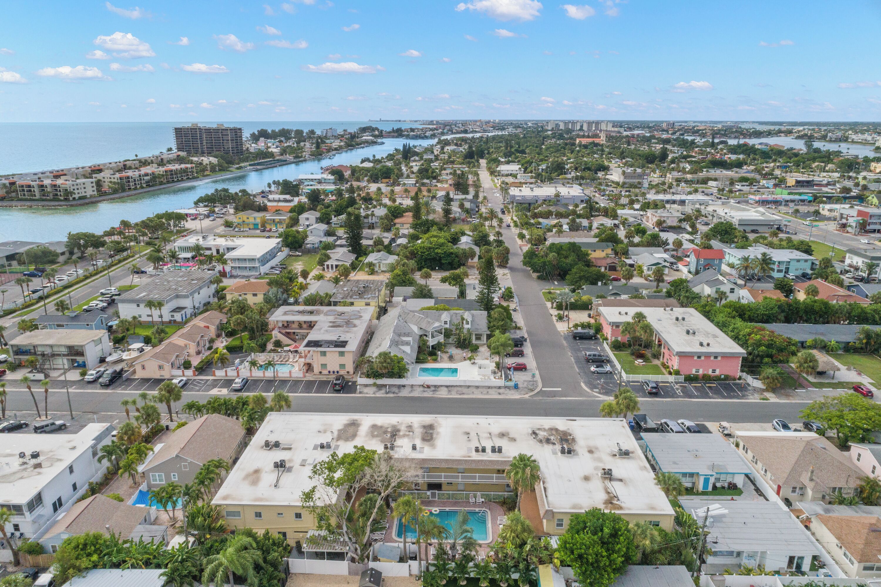 An aerial view of a coastal town with a marina, residential buildings, and a large hotel with a swimming pool.