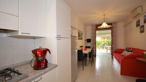 Una cocina moderna con armarios blancos, una cafetera roja y un comedor con sofá rojo y una mesa.