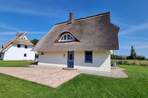 Situated on a well-maintained lawn, this charming cottage features a traditional thatched roof and a single entrance door.