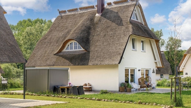 Uma casa com telhado de palha, área de estar coberta ao ar livre e um jardim bem cuidado.
