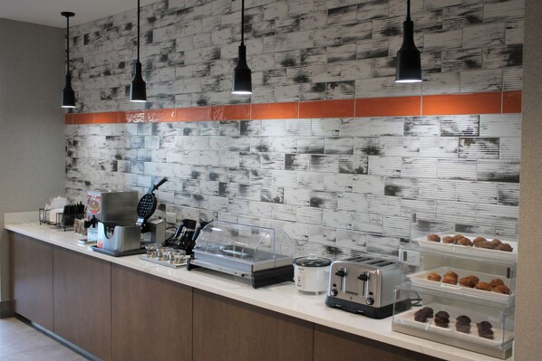 A breakfast bar with a coffee machine, toaster, and various pastries.
