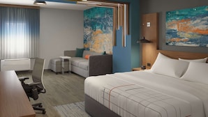 A modern hotel room with a large bed, a desk, a sofa, and a chair. There are two paintings on the walls and a window with curtains. - La Quinta Inn & Suites by Wyndham Bardstown (Bardstown)