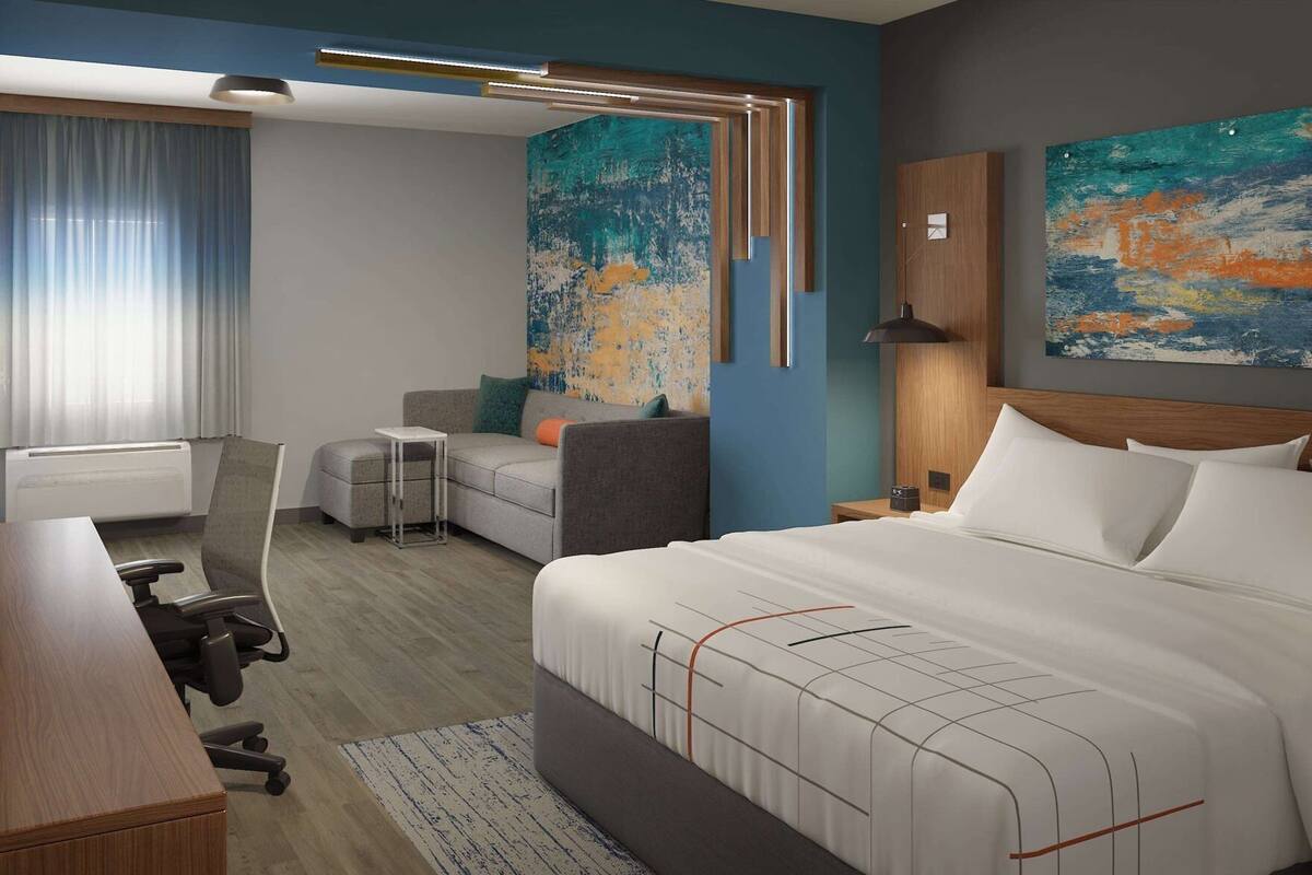 Habitació d'hotel amb un llit gran, una escriptori, una cadira, una taula petita i un sofà. Hi ha dos quadres a les parets.