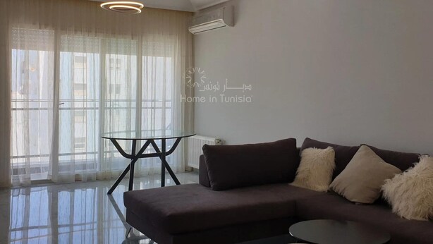 A modern living room with a dark brown sofa, a glass coffee table, and sheer curtains on a large window. - Lovely, apparently feet in the water (sousse)